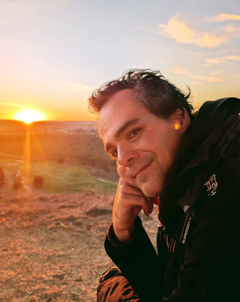Photograph of a middle-aged white dude smiling at the camera, taken at sunset